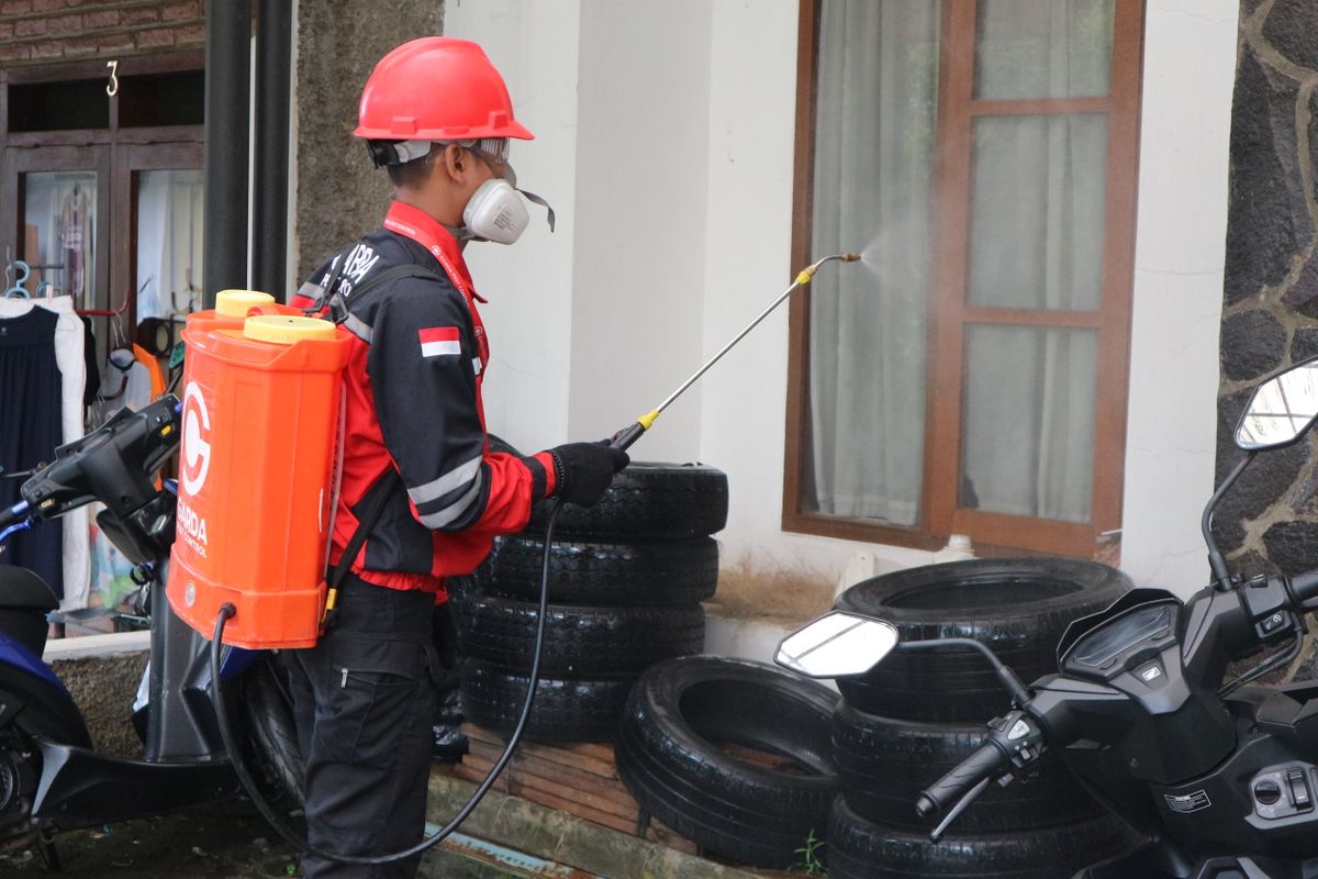 Licensed pest technician applying a perimeter treatment to the outside of a brick home