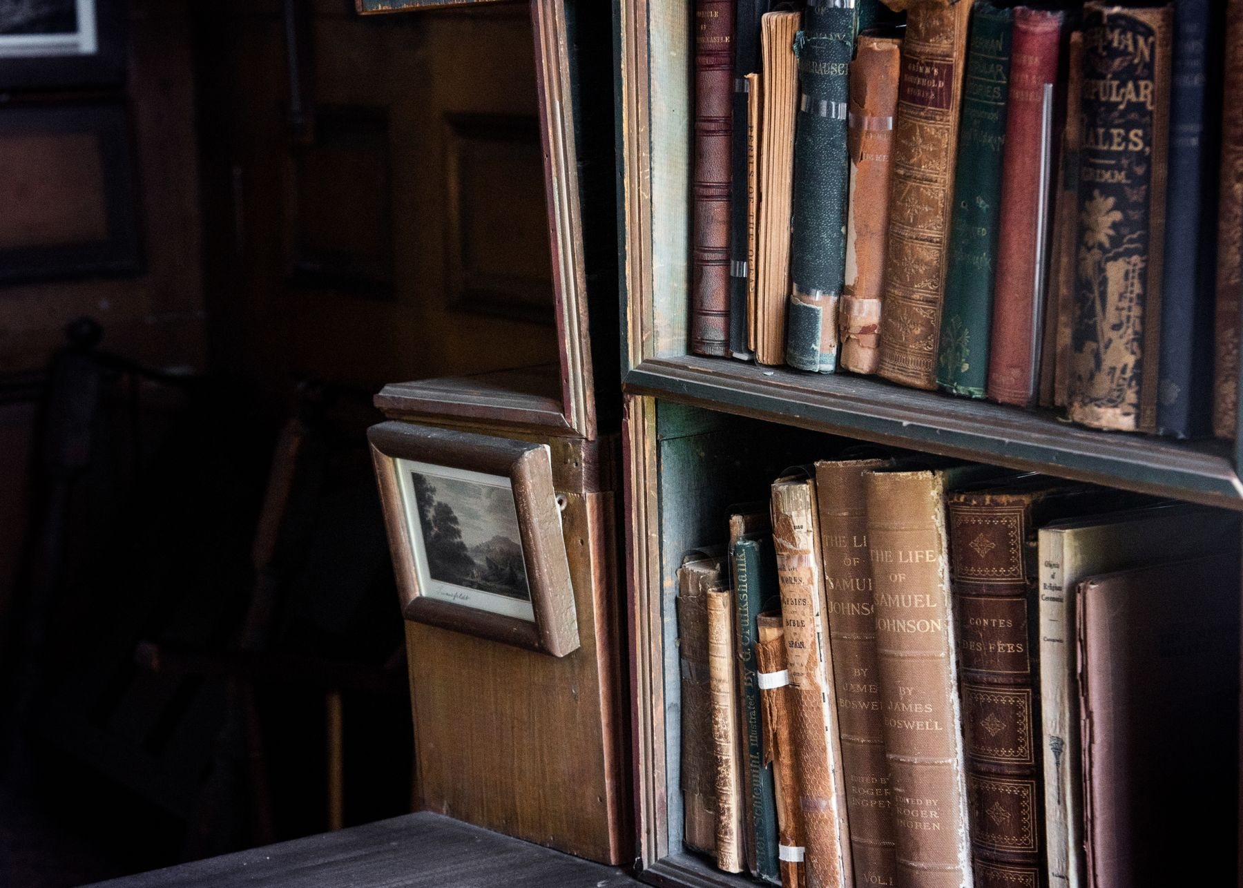 Old leather-bound books on a wooden bookshelf in a dim room